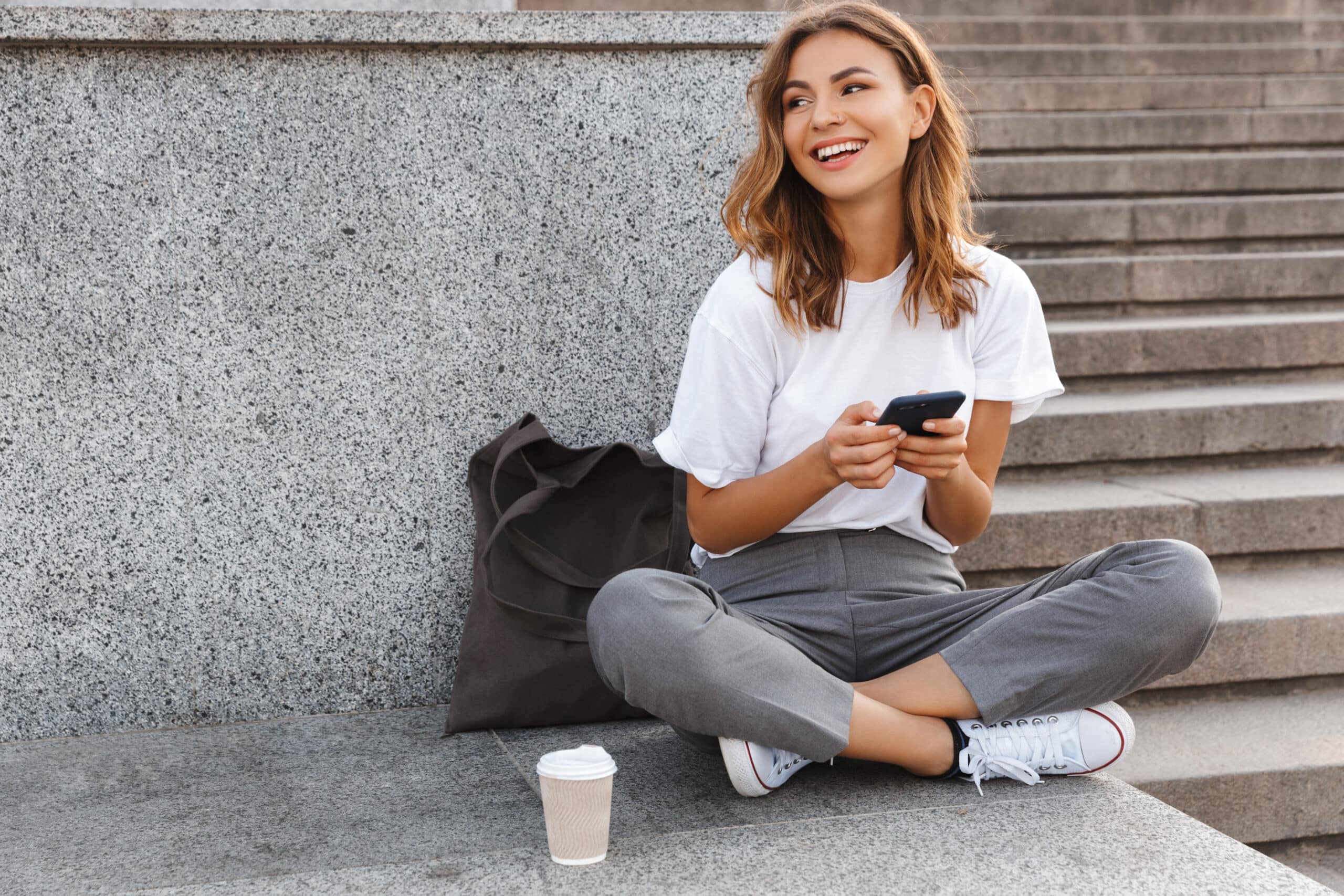 Girl sitting cross-legged outdoors holding a phone