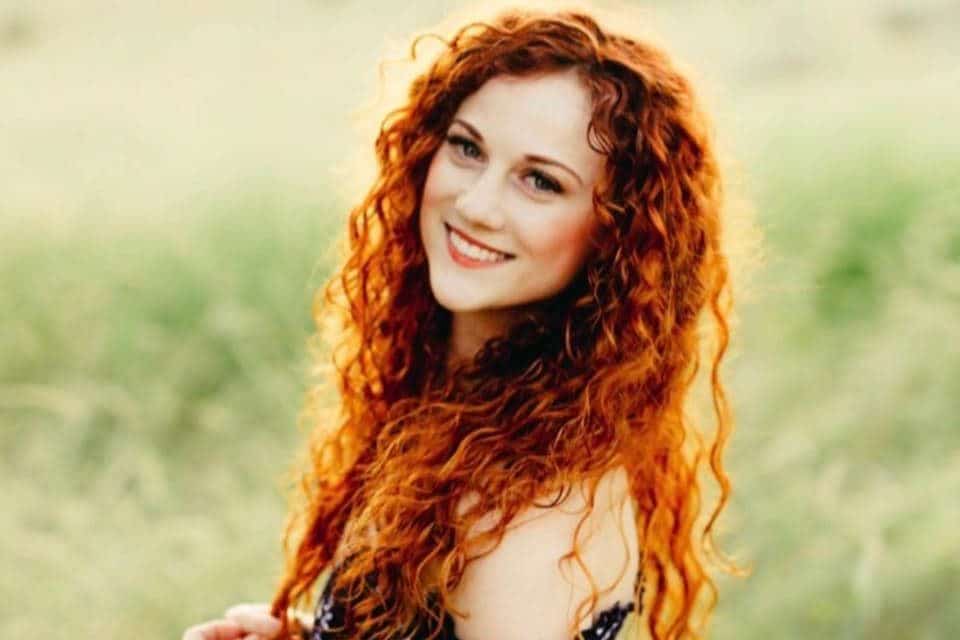 Collete Hood - An Aveda Alumni portriat of her in a green grass field wearing a dress and red long curly hair