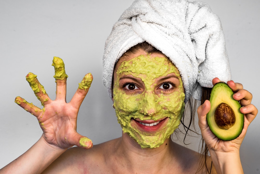 woman holding avacado with green face mask