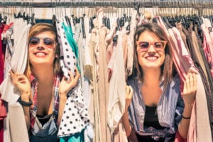 two friends smiling peeking through a rack of clothes