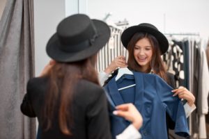 woman in black hat shopping and looking in mirror holding a jacket