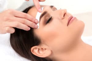 placing wax strip above woman's eyebrow
