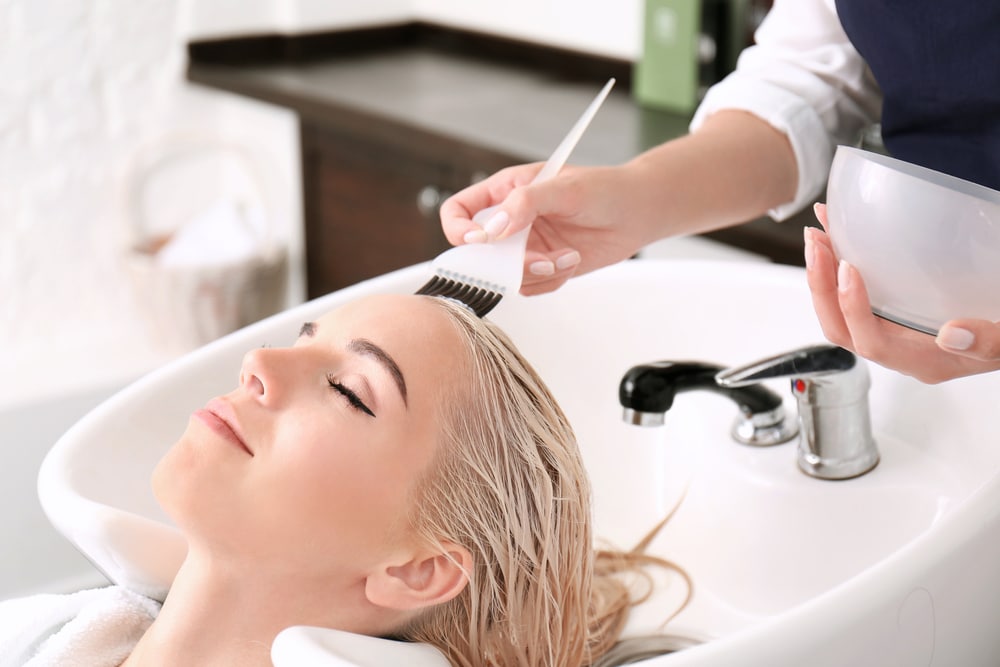 hairstylist touching up platnum blonde's hair while washing it