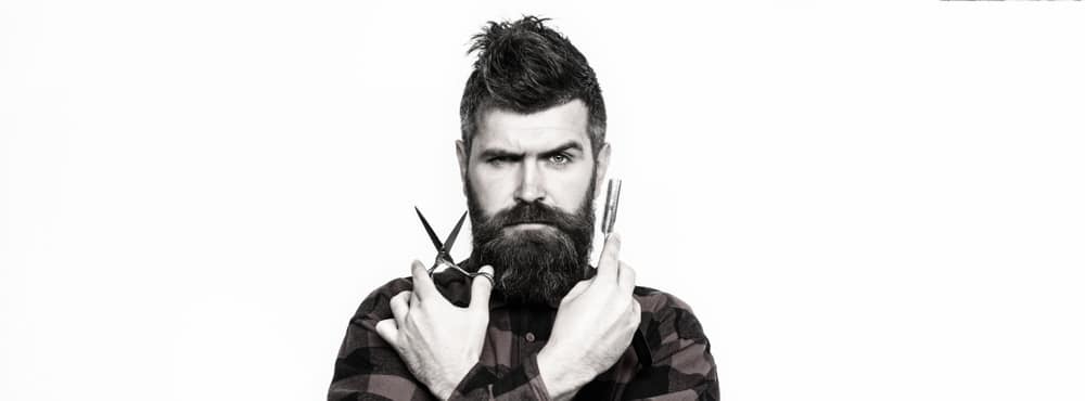 Black and white picture with male barber facing camera holding scissors in one hand and razor in the other