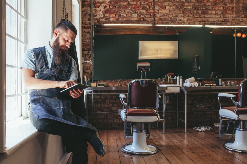 Male barber in barber shop looking at an ipad.