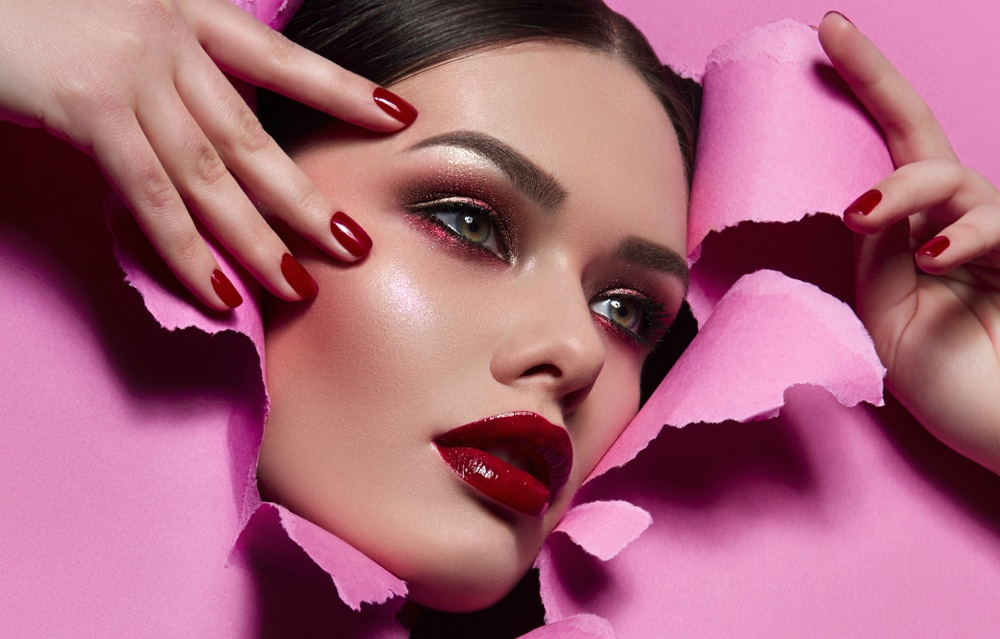 done up brunette model sticking her head through a hot pink ripped paper