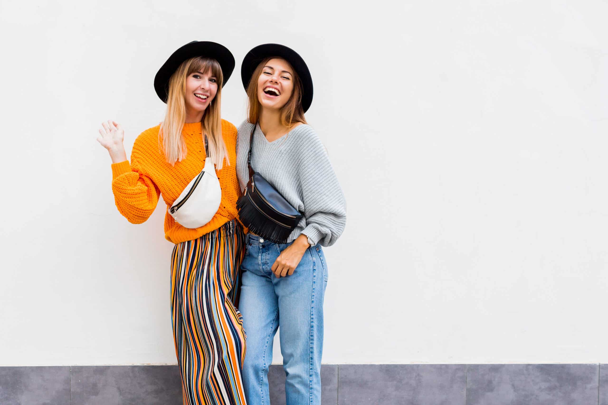 two trendy girl friends laughing and hugging with fanny packs
