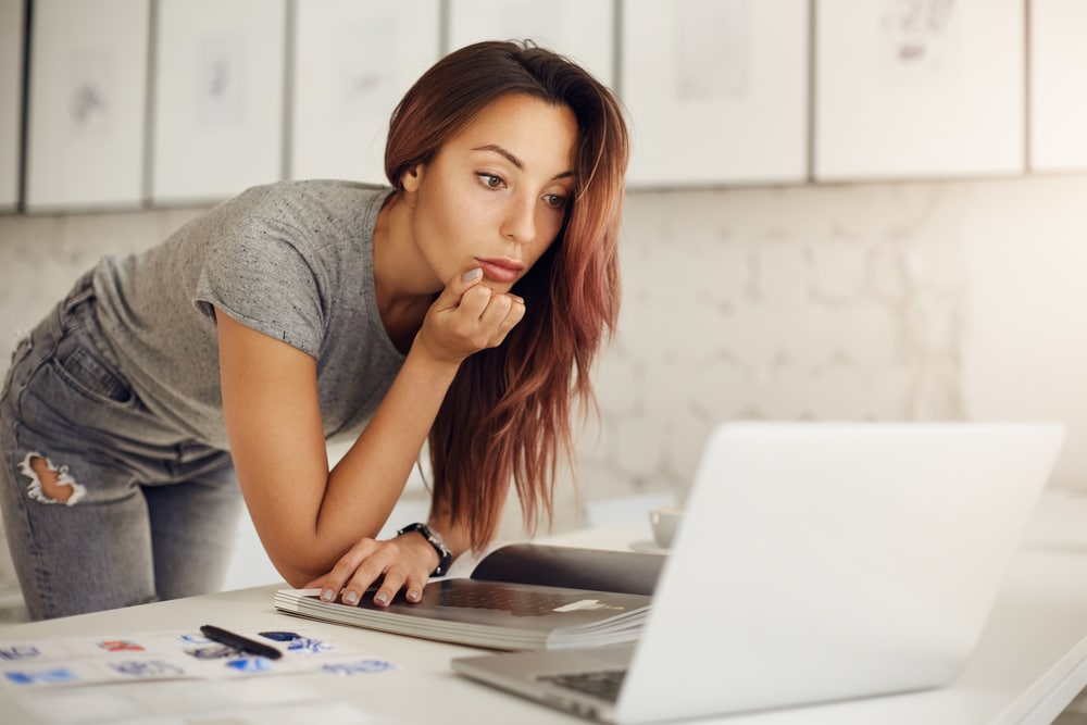 trendy girl with pink hair looking at her laptop on the desk