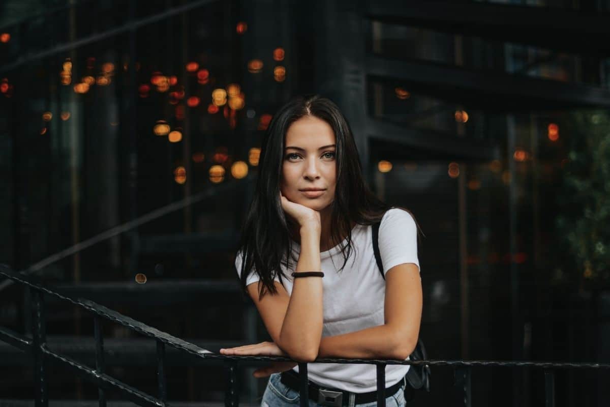 brunette woman in a white shirt leaning on a railing